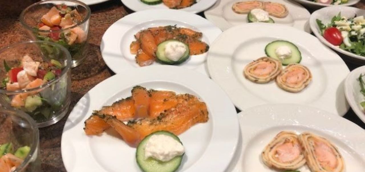 Teller mit Lachs, Gurkenscheiben und Sahne. Daneben Gläser mit Salat und Teller mit Lachsrollen. Frühstücksbuffet mit frischen Zutaten., © Kronen Hotel GmbH