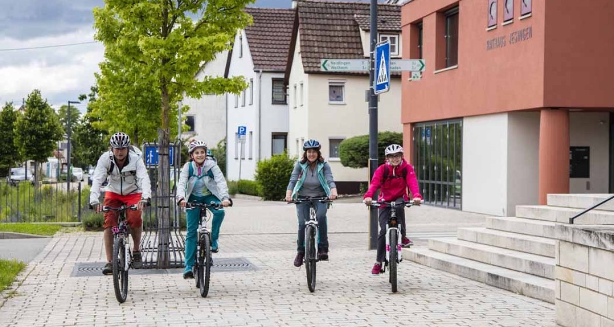 Vier Radfahrer fahren auf einem gepflasterten Weg in einer Wohngegend, vorbei am Rathaus Jesingen., © Schwäbische Alb Tourismusverband e.V. Vier Radfahrer fahren auf einem gepflasterten Weg in einer Wohngegend, vorbei am Rathaus Jesingen., © Schwäbische Alb Tourismusverband e.V.
