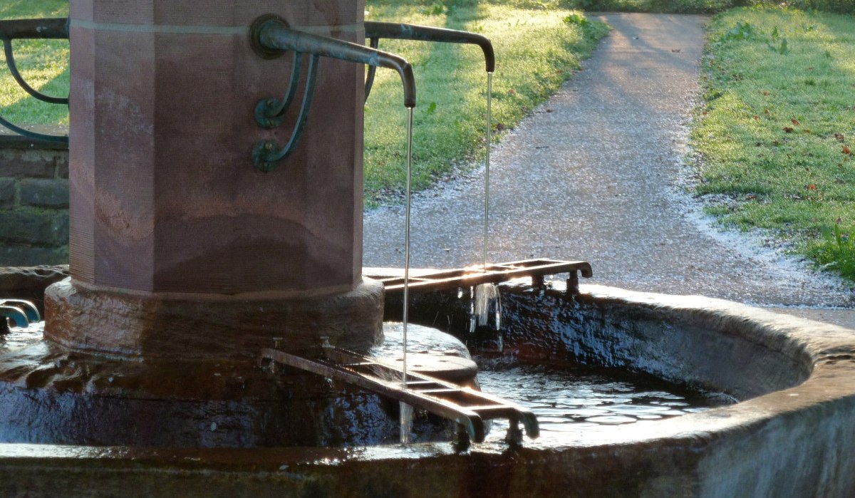 Ein alter Brunnen mit fließendem Wasser in einem Park. Ein Weg führt durch die grüne Landschaft, beleuchtet von der Morgensonne., © Landkreis Göppingen Ein alter Brunnen mit fließendem Wasser in einem Park. Ein Weg führt durch die grüne Landschaft, beleuchtet von der Morgensonne., © Landkreis Göppingen