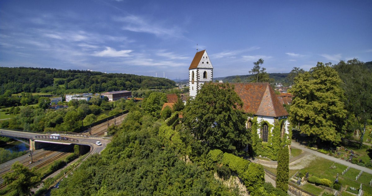 Luftaufnahme der Stadtkirche St Blasius, umgeben von Bäumen und einem Friedhof, mit einer Straße und Eisenbahnschienen im Vordergrund., © Pressel-Fotodesign