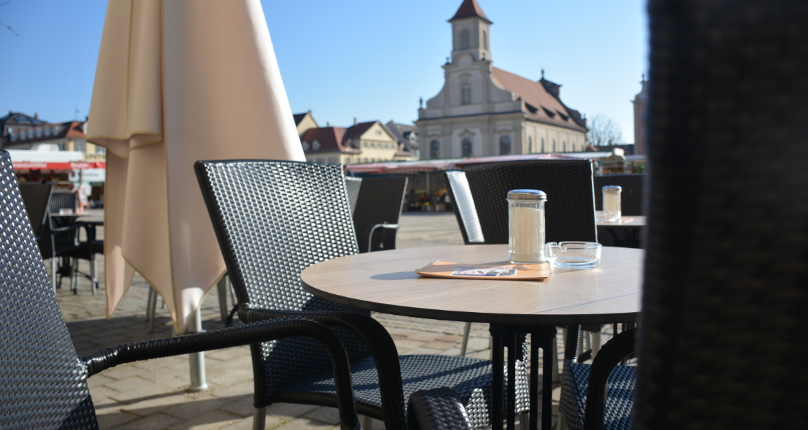 Leerer Außenbereich eines Cafés mit Tischen und Stühlen, im Hintergrund eine Kirche bei klarem Himmel., © Konditorei Lutz