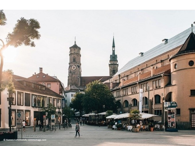 Die Stuttgarter Markthalle bei Sonnenuntergang, umgeben von historischen Gebäuden und einem belebten Platz mit Menschen und Cafés., © Stuttgart Marketing GmbH Die Stuttgarter Markthalle bei Sonnenuntergang, umgeben von historischen Gebäuden und einem belebten Platz mit Menschen und Cafés., © Stuttgart Marketing GmbH