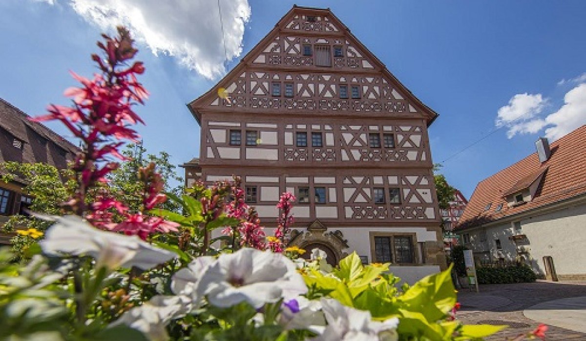 Fachwerkhaus mit reich verziertem Giebel, umgeben von blühenden Blumen im Vordergrund. Der Himmel ist blau mit einigen Wolken., © Achim Mende Fachwerkhaus mit reich verziertem Giebel, umgeben von blühenden Blumen im Vordergrund. Der Himmel ist blau mit einigen Wolken., © Achim Mende