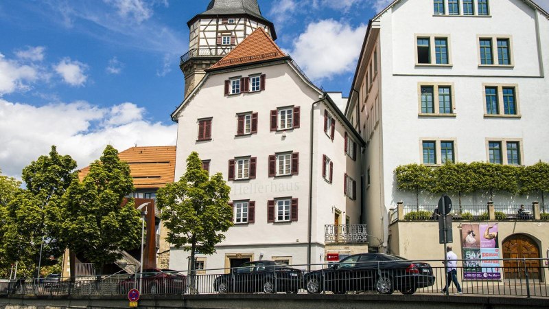 Bandhaus und Helferhaus in Backnang bei sonnigem Wetter mit weißer Fassade, Fachwerkturm und Bäumen davor., © SMG, Sarah Schmid Bandhaus und Helferhaus in Backnang bei sonnigem Wetter mit weißer Fassade, Fachwerkturm und Bäumen davor., © SMG, Sarah Schmid