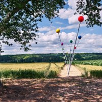 Bunte Kugeln auf langen Stangen ragen in einem Feld in die Höhe, daneben ein großer Baum. Der Himmel ist bewölkt., © Natur.Nah. Schönbuch & Heckengäu