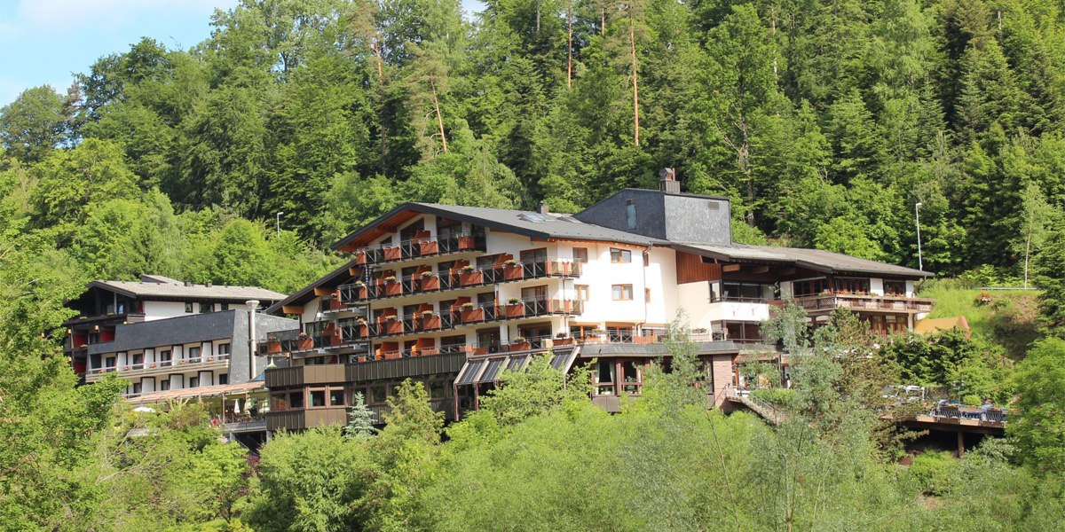 Ein großes Hotel im Wald mit mehreren Balkonen, umgeben von üppigem Grün und Bäumen., © Ringhotel Mönchs Waldhotel