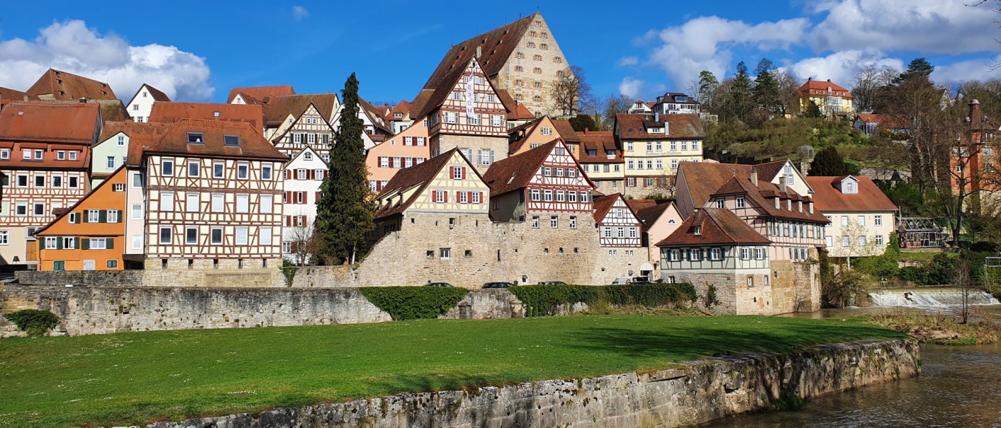 Fachwerkhäuser in Schwäbisch Hall, umgeben von grünen Wiesen und einem Fluss, unter blauem Himmel mit einigen Wolken., © Stadt Schwäbisch Hall Fachwerkhäuser in Schwäbisch Hall, umgeben von grünen Wiesen und einem Fluss, unter blauem Himmel mit einigen Wolken., © Stadt Schwäbisch Hall