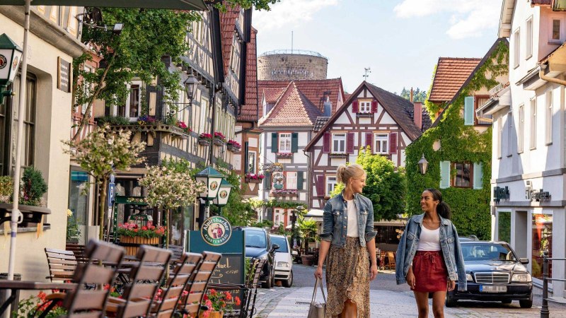 Blick die Kirchstraße mit ihren Fachwerkhäusern entlang auf den gemauerten Waldhornturm. Zwei Frauen flanieren durch die Straße., © SMG, Martina Denker