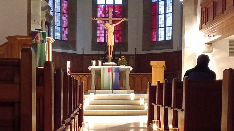Blick in den Chor der Stadtkirche mit Altar, Kruzifix und gotischen Glasfenstern, im Vordergrund dunkelbraune Kirchenbänke rechts und links vom Mittelgang, © Petra Natzkowski