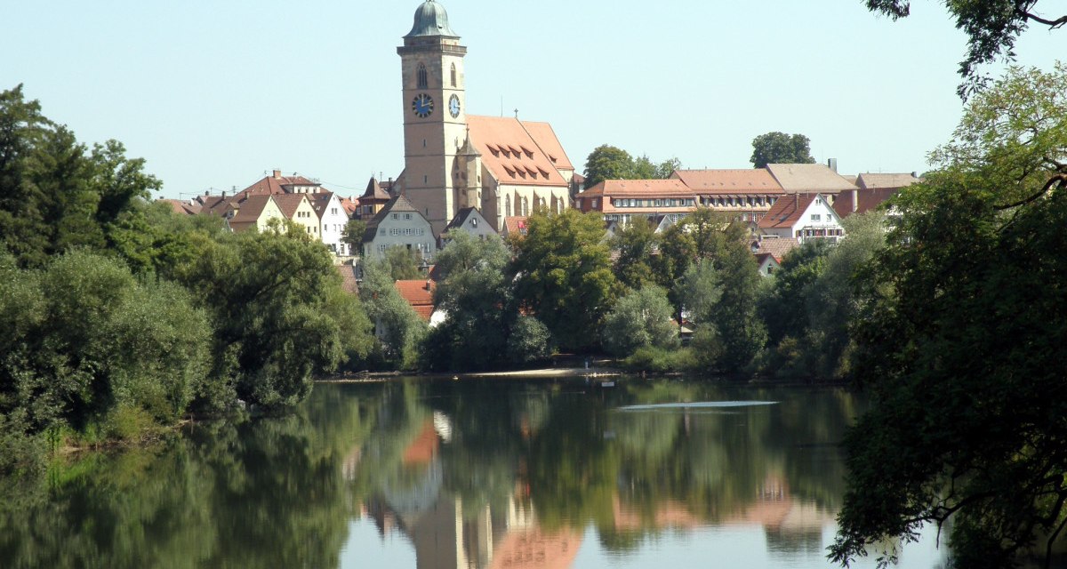 Nürtingen am Neckar mit einer Kirche im Zentrum, umgeben von Bäumen. Die Spiegelung der Stadt ist im ruhigen Wasser sichtbar., © Stadt Nürtingen