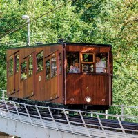 Eine historische Standseilbahn mit Holzverkleidung fährt eine geneigte Strecke entlang, umgeben von dichtem Grün., © TMBW, Gregor Lengler