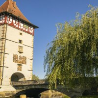 Das Beinsteiner Tor in Waiblingen mit Fachwerk und Brücke, umgeben von Bäumen, unter klarem Himmel., © SMG, Sarah Schmid Das Beinsteiner Tor in Waiblingen mit Fachwerk und Brücke, umgeben von Bäumen, unter klarem Himmel., © SMG, Sarah Schmid