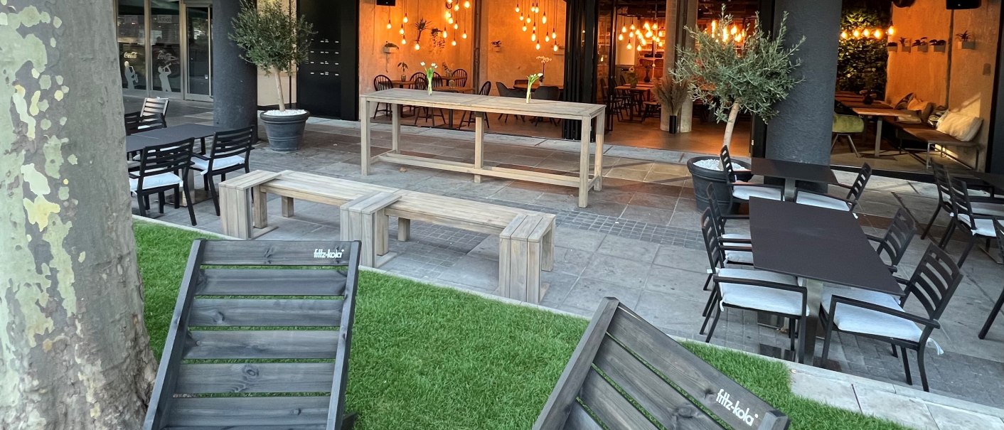 Gemütlicher Außenbereich mit Holzmöbeln, Rasenfläche und Lichterketten. Innenbereich mit warmem Licht sichtbar., © heavenskitchen