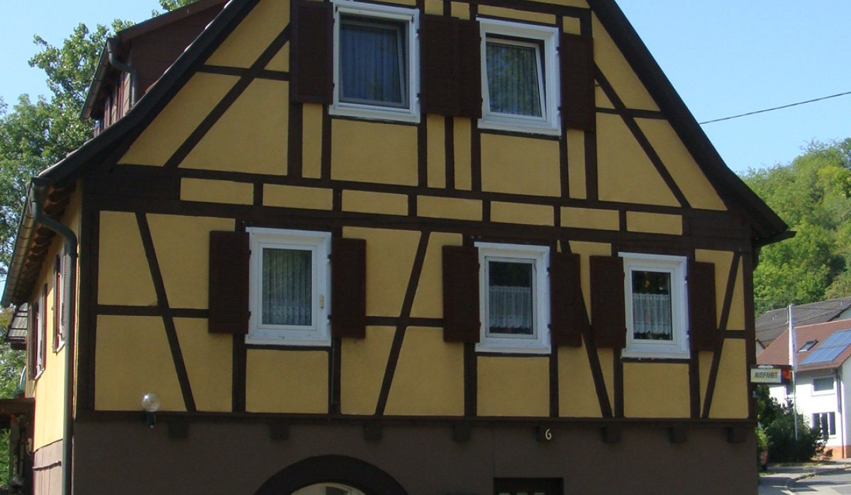 Fachwerkhaus mit gelber Fassade und braunen Balken, an einer Straße gelegen. Vor dem Haus stehen Pflanzen in Töpfen., © Land der 1000 Hügel - Kraichgau-Stromberg