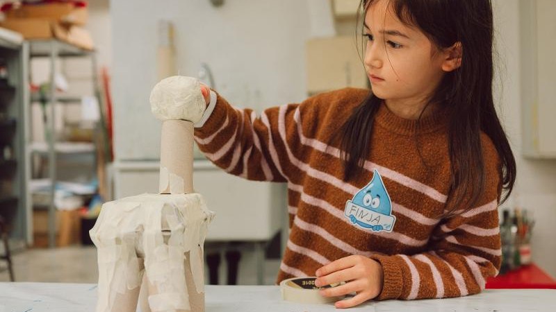 Ein Kind bastelt konzentriert mit Papprollen und Klebeband an einem Tisch in einem Workshop-Raum., © Kunstschule Labyrinth Ein Kind bastelt konzentriert mit Papprollen und Klebeband an einem Tisch in einem Workshop-Raum., © Kunstschule Labyrinth