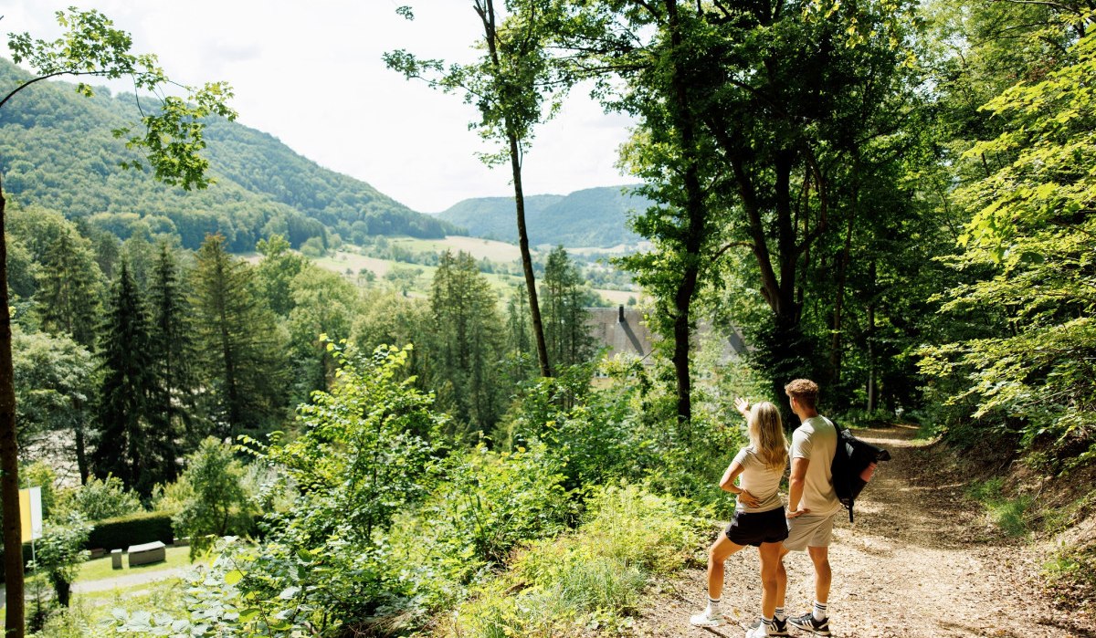 Zwei Personen wandern auf einem Waldweg mit Blick auf eine grüne, hügelige Landschaft. Sie genießen die Aussicht auf Wälder und Täler., © Landkreis Göppingen