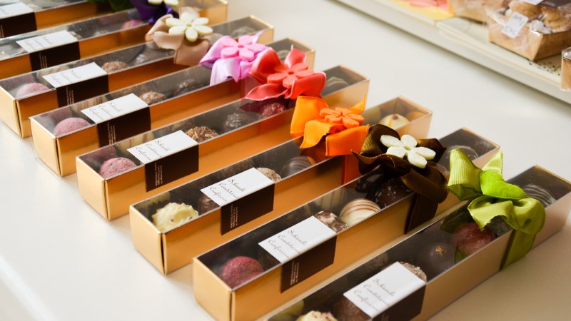 Elegante Pralinenboxen mit bunten Schleifen in einer Reihe angeordnet. Jede Box enthält eine Auswahl an Schokoladenpralinen., © Schümli Elegante Pralinenboxen mit bunten Schleifen in einer Reihe angeordnet. Jede Box enthält eine Auswahl an Schokoladenpralinen., © Schümli