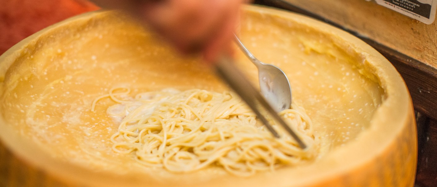 Spaghetti werden in einem ausgehöhlten Parmesanlaib mit einem Löffel gemischt. Der Käse dient als Schüssel und verleiht den Nudeln Geschmack., © La Signora Moro Spaghetti werden in einem ausgehöhlten Parmesanlaib mit einem Löffel gemischt. Der Käse dient als Schüssel und verleiht den Nudeln Geschmack., © La Signora Moro