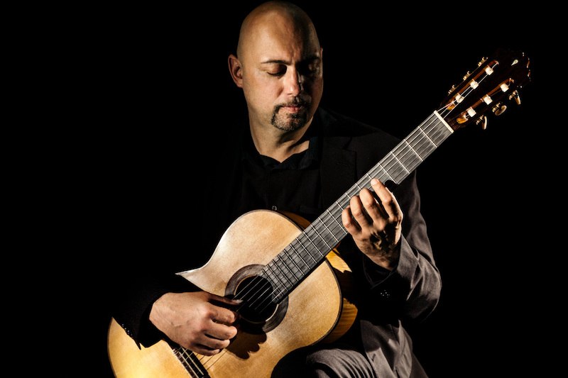 Ein Mann in dunkler Kleidung spielt konzentriert auf einer klassischen Gitarre vor schwarzem Hintergrund., © Stadtverwaltung Vaihingen an der Enz Ein Mann in dunkler Kleidung spielt konzentriert auf einer klassischen Gitarre vor schwarzem Hintergrund., © Stadtverwaltung Vaihingen an der Enz