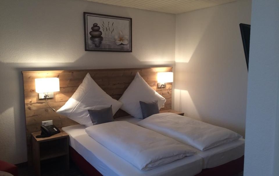 Gemütliches Doppelzimmer mit Holzkopfteil, zwei Kissen, zwei Nachttischen und einem Bild an der Wand., © Hotel Lamm Hegnach