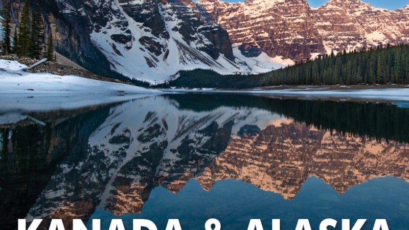 Schneebedeckte Berge spiegeln sich in einem ruhigen See. Text: Kanada & Alaska Into the Wild., © Expedition Erde