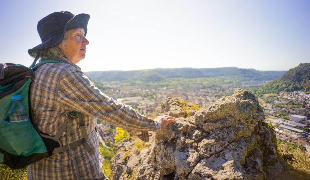 Person mit Hut und Rucksack steht auf einem Felsen und blickt auf eine weite Landschaft mit Hügeln und Stadt im Hintergrund., © Stadt Geislingen an der Steige Person mit Hut und Rucksack steht auf einem Felsen und blickt auf eine weite Landschaft mit Hügeln und Stadt im Hintergrund., © Stadt Geislingen an der Steige