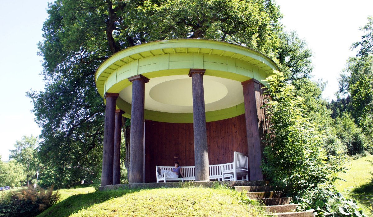Ein runder Pavillon mit Säulen und weißen Bänken steht auf einem Hügel in einem grünen Park., © Landkreis Göppingen