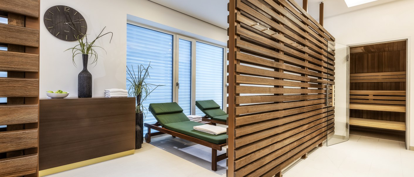 Moderner Wellnessbereich mit zwei grünen Liegen, einer Sauna und Holzelementen. Eine Vase mit Pflanzen und eine Wanduhr ergänzen das Ambiente., © Mövenpick Hotel Stuttgart Messe & Congress Moderner Wellnessbereich mit zwei grünen Liegen, einer Sauna und Holzelementen. Eine Vase mit Pflanzen und eine Wanduhr ergänzen das Ambiente., © Mövenpick Hotel Stuttgart Messe & Congress