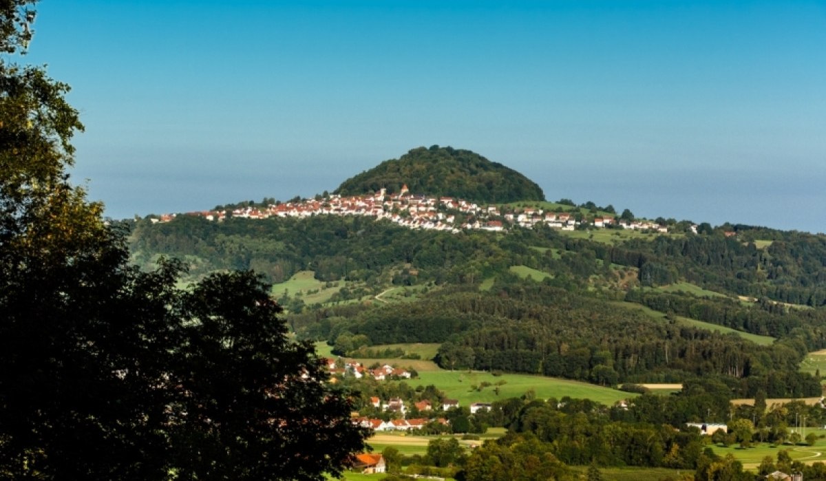 Der Hohenstaufen erhebt sich majestätisch über die umliegende Landschaft, umgeben von grünen Wäldern und kleinen Dörfern unter einem klaren blauen Himmel., © Landratsamt Göppingen Der Hohenstaufen erhebt sich majestätisch über die umliegende Landschaft, umgeben von grünen Wäldern und kleinen Dörfern unter einem klaren blauen Himmel., © Landratsamt Göppingen