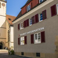 Gebäude mit der Aufschrift 'Tourist Information' neben einer Kirche mit Turm und roten Fensterläden, bei sonnigem Wetter., © Stuttgart-Marketing GmbH, Sarah Schmid Gebäude mit der Aufschrift 'Tourist Information' neben einer Kirche mit Turm und roten Fensterläden, bei sonnigem Wetter., © Stuttgart-Marketing GmbH, Sarah Schmid