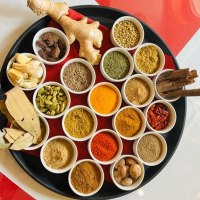 Ein rundes Tablett mit verschiedenen Gewürzen in kleinen Schalen, darunter Ingwer, Knoblauch, Zimtstangen und bunte Gewürzpulver., © Sangam Ein rundes Tablett mit verschiedenen Gewürzen in kleinen Schalen, darunter Ingwer, Knoblauch, Zimtstangen und bunte Gewürzpulver., © Sangam