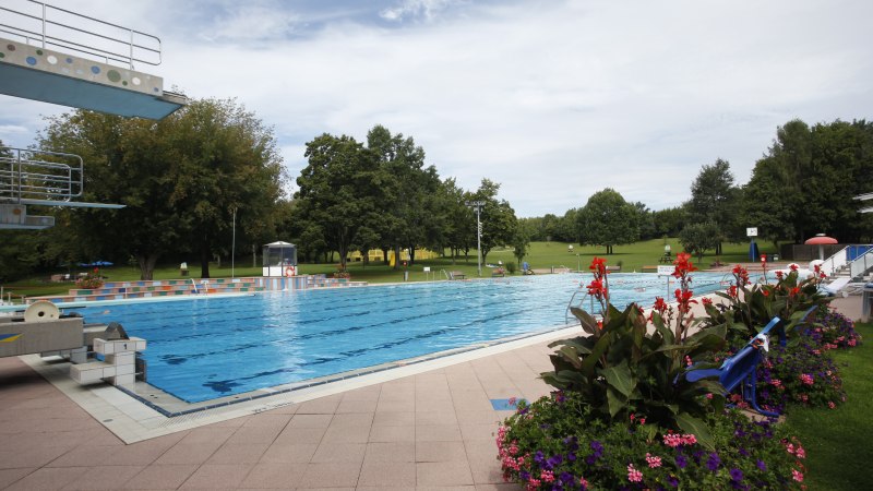 Ein Freibad mit einem großen Schwimmbecken, umgeben von grünen Bäumen und bunten Blumenbeeten. Der Himmel ist leicht bewölkt., © Stuttgarter Bäder Ein Freibad mit einem großen Schwimmbecken, umgeben von grünen Bäumen und bunten Blumenbeeten. Der Himmel ist leicht bewölkt., © Stuttgarter Bäder