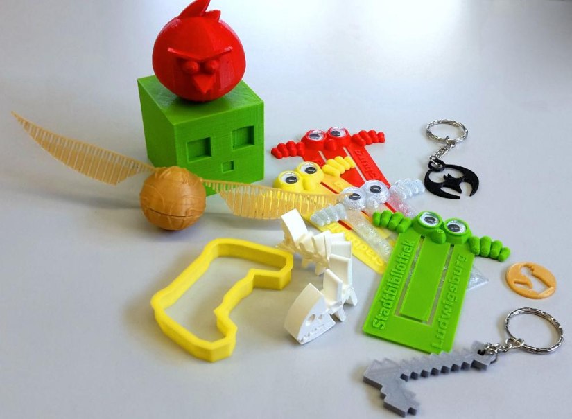 Bunte 3D-gedruckte Objekte auf einem Tisch, darunter ein roter Vogel, ein gr&uuml;ner W&uuml;rfel, Lineale mit Augen und verschiedene Schl&uuml;sselanh&auml;nger., &copy; Stadtbibliothek Ludwigsburg