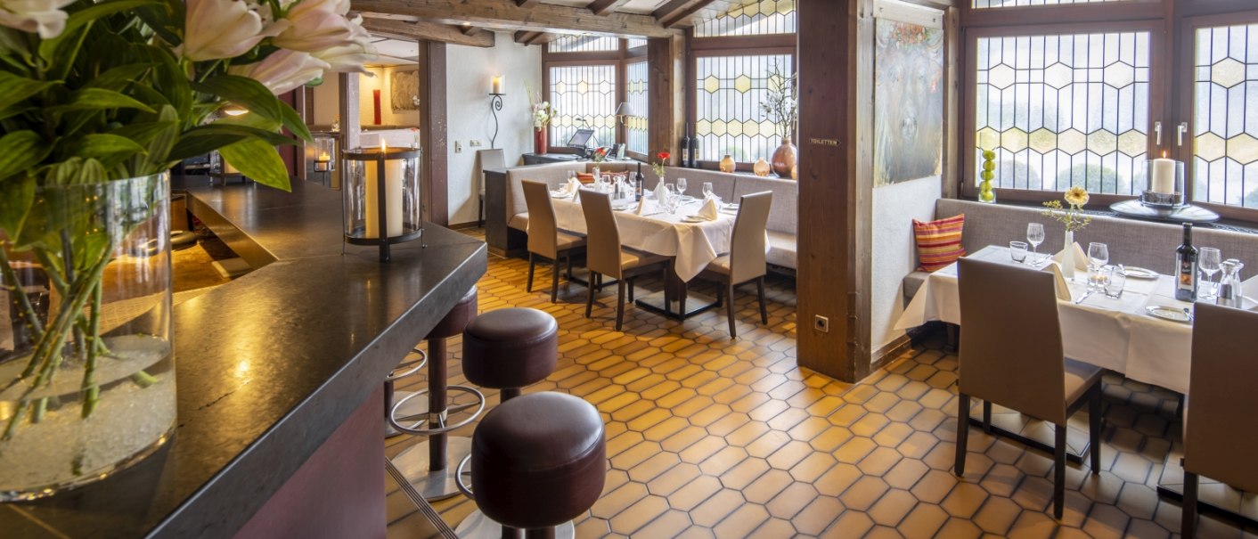 Ein gem&uuml;tliches Restaurant mit Holzbalkendecke, gedeckten Tischen und gro&szlig;en Fenstern. Blumen und Kerzen sorgen f&uuml;r eine einladende Atmosph&auml;re., &copy; Hotel Gloria GmbH