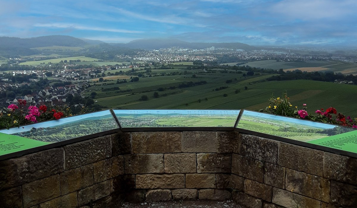 Aussichtspunkt mit Panoramatafeln, Blick auf Felder und eine Stadt in der Ferne. Blumen schmücken den Rand, blauer Himmel im Hintergrund., © Remstal Tourismus e.V. Aussichtspunkt mit Panoramatafeln, Blick auf Felder und eine Stadt in der Ferne. Blumen schmücken den Rand, blauer Himmel im Hintergrund., © Remstal Tourismus e.V.