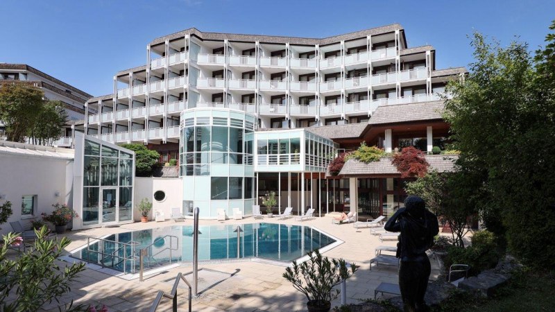 Ein modernes Hotel mit mehreren Etagen und Balkonen. Im Vordergrund ein Pool und eine Terrasse mit Liegestühlen, umgeben von Pflanzen., © Reha-Klinik Schwäbische Alb Ein modernes Hotel mit mehreren Etagen und Balkonen. Im Vordergrund ein Pool und eine Terrasse mit Liegestühlen, umgeben von Pflanzen., © Reha-Klinik Schwäbische Alb