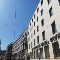Ein modernes Gebäude mit dem Schriftzug 'Hotel Royal' unter blauem Himmel. Die Straße ist von weiteren Gebäuden gesäumt., © Hotel Royal