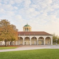 Historisches Gebäude mit Kuppel und Bögen, umgeben von herbstlichen Bäumen und gepflegtem Rasen., © Simon Sommer Historisches Gebäude mit Kuppel und Bögen, umgeben von herbstlichen Bäumen und gepflegtem Rasen., © Simon Sommer