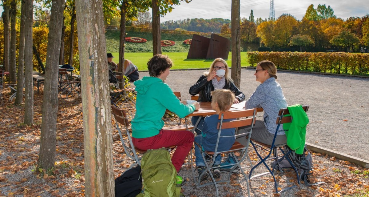 Menschen sitzen im Biergarten Steiner am Fluss, umgeben von Bäumen und Herbstlaub, bei sonnigem Wetter., © Bildergalerie Attila Menschen sitzen im Biergarten Steiner am Fluss, umgeben von Bäumen und Herbstlaub, bei sonnigem Wetter., © Bildergalerie Attila