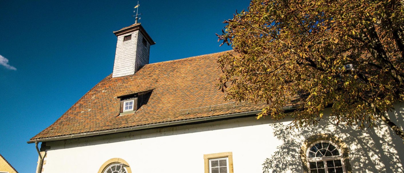 Die Peterskirche in Vaihingen an der Enz mit rotem Ziegeldach, kleinem Turm und einem Baum mit Herbstlaub vor blauem Himmel., © Stuttgart-Marketing GmbH, Sarah Schmid Die Peterskirche in Vaihingen an der Enz mit rotem Ziegeldach, kleinem Turm und einem Baum mit Herbstlaub vor blauem Himmel., © Stuttgart-Marketing GmbH, Sarah Schmid