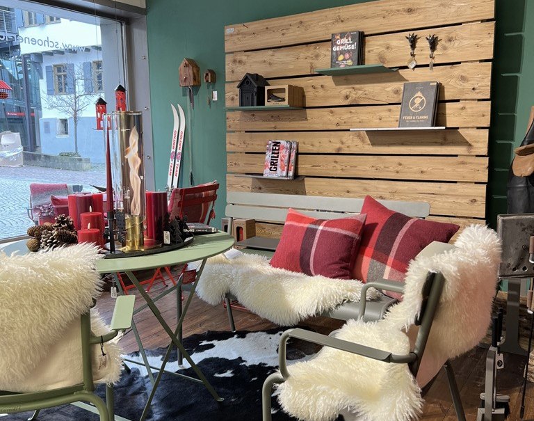 Gemütliche Ladenecke mit Tisch und Stühlen, dekoriert mit Fellen und Kissen. Holzwand mit Büchern und Dekoration. Blick nach draußen auf die Straße., © schöner laden
