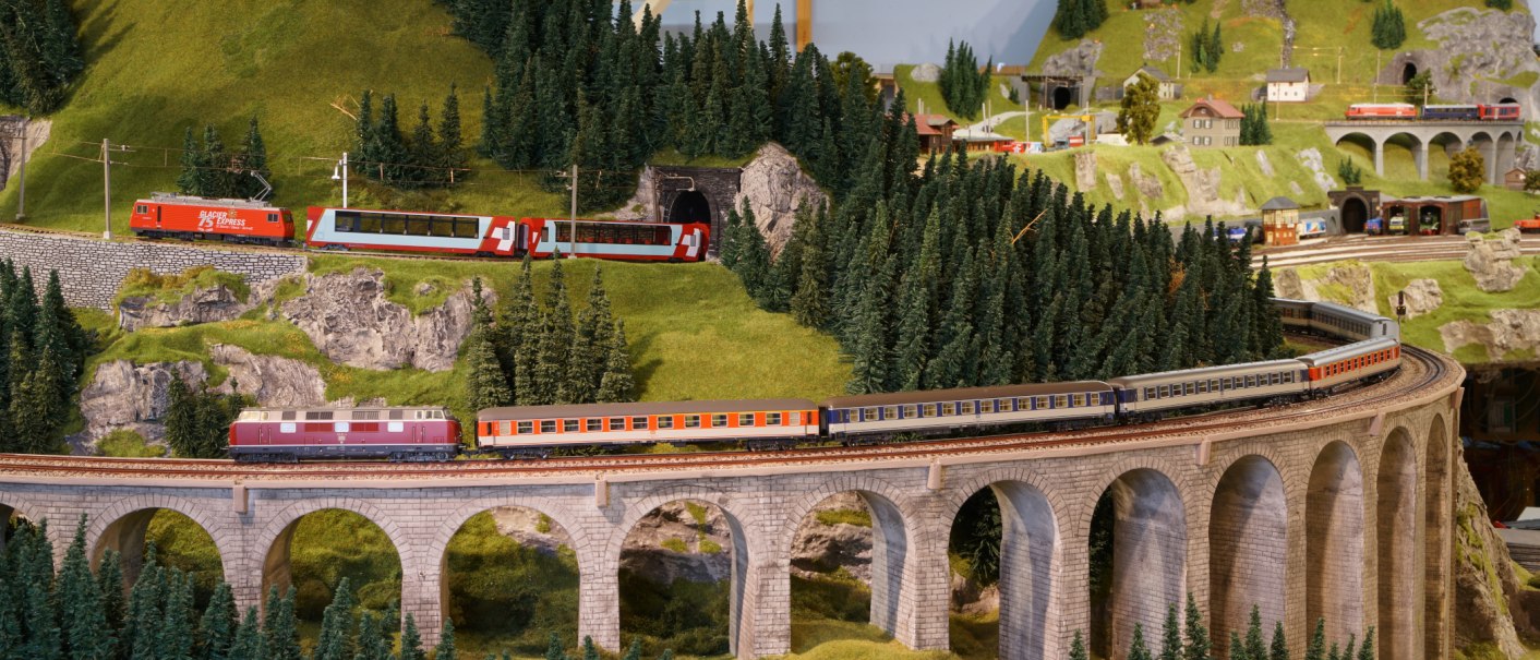 Modelleisenbahn mit Zügen auf einem Viadukt in einer bergigen Landschaft mit Tannen und kleinen Gebäuden. Detailreiche Miniaturszene., © PMW Winnenden e.V. Modelleisenbahn mit Zügen auf einem Viadukt in einer bergigen Landschaft mit Tannen und kleinen Gebäuden. Detailreiche Miniaturszene., © PMW Winnenden e.V.