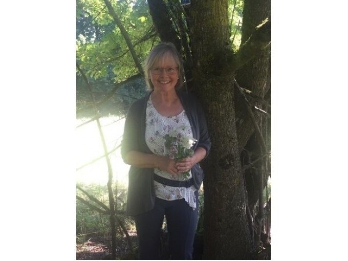 Eine Frau steht l&auml;chelnd neben einem Baum und h&auml;lt einen Strau&szlig; Wildkr&auml;uter. Sonnenlicht f&auml;llt durch die Bl&auml;tter und erzeugt ein angenehmes Lichtspiel., &copy; Touristik und Marketing GmbH