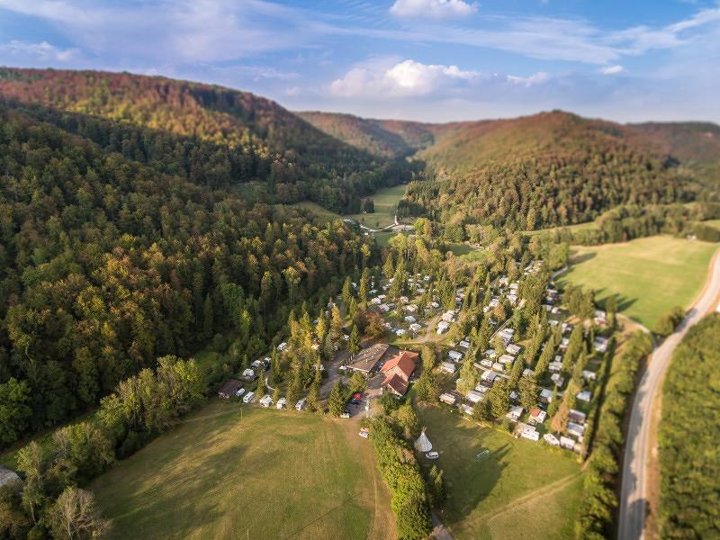Luftaufnahme des Campingplatzes Pfählhof in einem bewaldeten Tal mit Wohnwagen und Zelten, umgeben von Hügeln und einer Straße., © Campingplatz Pfählhof Luftaufnahme des Campingplatzes Pfählhof in einem bewaldeten Tal mit Wohnwagen und Zelten, umgeben von Hügeln und einer Straße., © Campingplatz Pfählhof