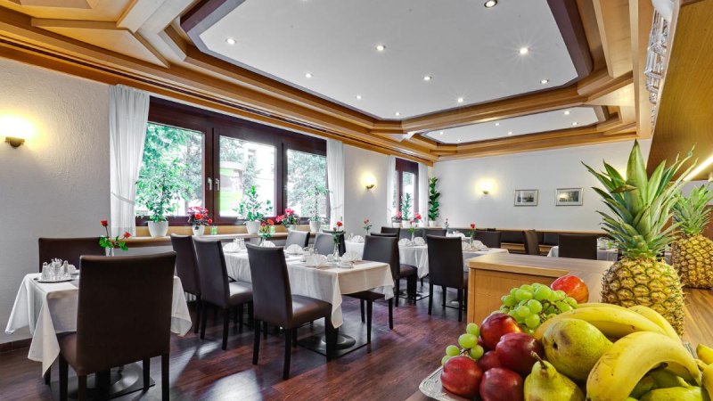 Eleganter Frühstücksraum mit gedeckten Tischen, dunklen Stühlen und einer Obstschale im Vordergrund. Große Fenster lassen viel Licht herein., © ARNOTEL GmbH