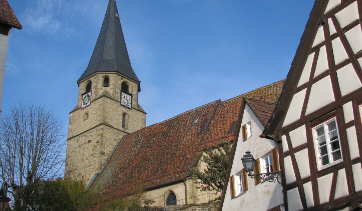 Die Sankt Martinskirche mit ihrem markanten Turm steht neben Fachwerkhäusern unter einem klaren blauen Himmel., © Land der 1000 Hügel - Kraichgau-Stromberg