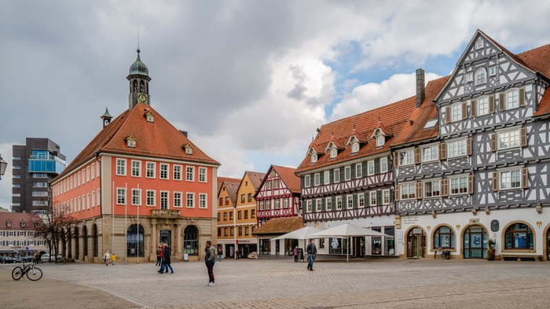 Der Marktplatz in Schorndorf zeigt historische Fachwerkhäuser und ein rotes Gebäude mit Turm. Menschen spazieren über den Platz. Der Marktplatz in Schorndorf zeigt historische Fachwerkhäuser und ein rotes Gebäude mit Turm. Menschen spazieren über den Platz.