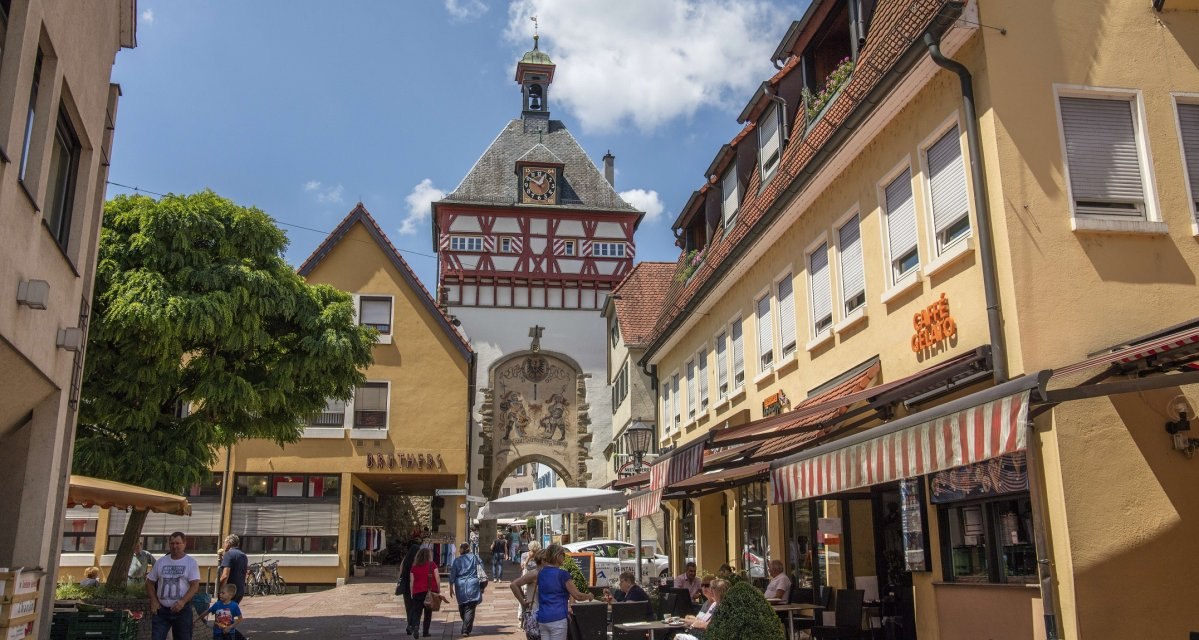 Stra&szlig;enszene in einer Altstadt mit Fachwerkhaus und Uhrturm. Menschen flanieren und sitzen in Stra&szlig;encaf&eacute;s. Der Himmel ist blau mit wenigen Wolken., &copy; Stuttgart Marketing GmbH Achim Mende