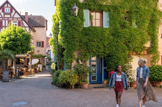 Zwei Frauen spazieren durch eine malerische Altstadt mit Fachwerkhäusern und begrünten Fassaden., © Stadt Besigheim Zwei Frauen spazieren durch eine malerische Altstadt mit Fachwerkhäusern und begrünten Fassaden., © Stadt Besigheim
