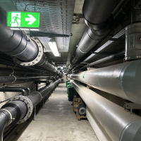 Ein unterirdischer Technikgang mit gro&szlig;en Rohren und einem leuchtenden Notausgangsschild an der Decke., &copy; Stadtwerke Ludwigsburg-Kornwestheim GmbH